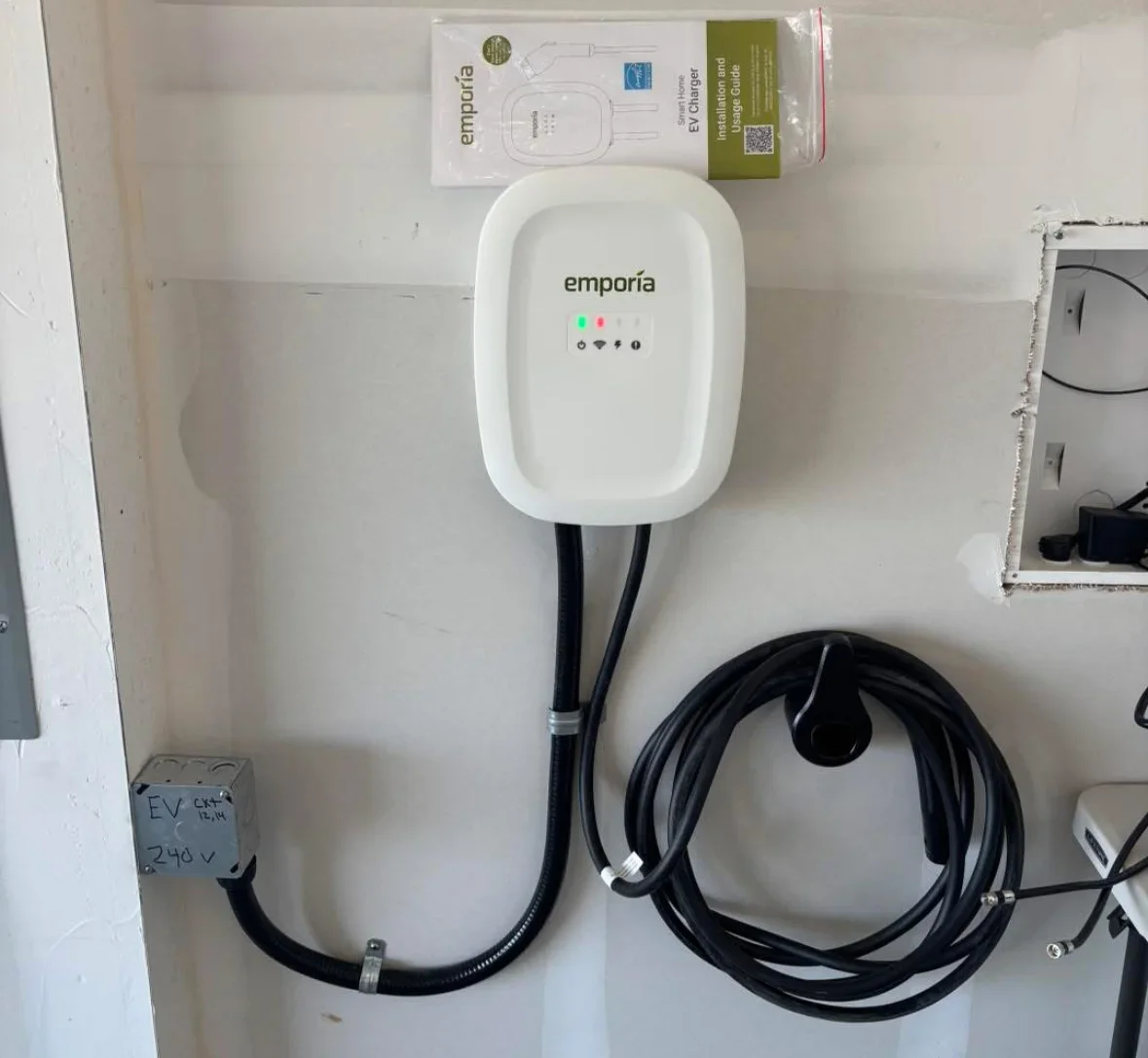 White Emporía EV charger mounted on wall with black charging cable and 240V circuit connection