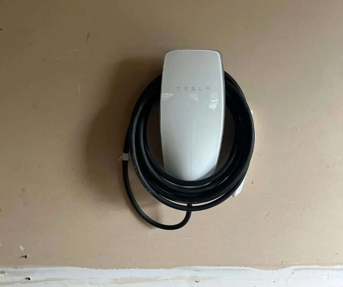 White Tesla Wall Connector mounted on drywall with black coiled charging cable